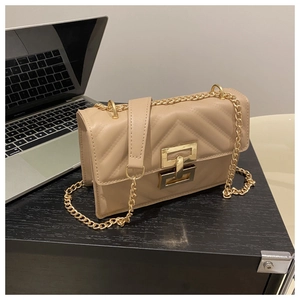 Detail of beige quilted shoulder bag with gold metal clasp and chain strap on desk