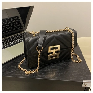 Detail of black quilted shoulder bag with gold chain strap and metal clasp on a wooden desk