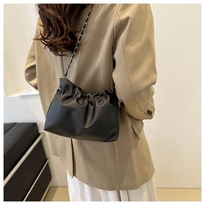 Detail of black pleated bucket bag with silver chain strap worn by a model