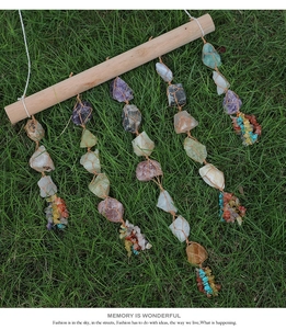 Detail of handmade wall hanging with raw crystals on a wooden stick over grass