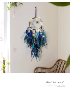 Detail of moon-shaped dreamcatcher with blue feathers and warm LED lights on white wall
