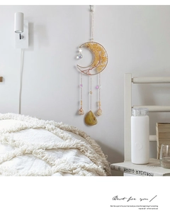 Detail of moon-shaped golden crystal suncatcher with raw stones on a white bedroom wall