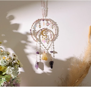 Detail of amethyst suncatcher with gold moon and star charms on white wall background
