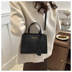 Detail of black square tote bag with gold logo lettering shown worn as a crossbody bag