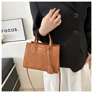 Detail of caramel faux leather handbag with gold lettering and adjustable strap