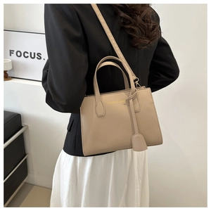 Detail of beige faux leather tote bag with gold lettering shown on shoulder with blazer