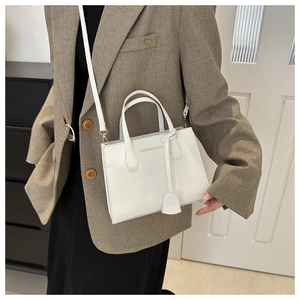 Chic white square crossbody bag with gold lettering shown on a stylish brown suit
