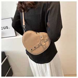 Chique beige hartvormige crossbodytas met zilveren studs gedragen door een model op wit