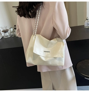 Elegante beige Schultertasche mit silberner Kette in einer stilvollen Café-Umgebung