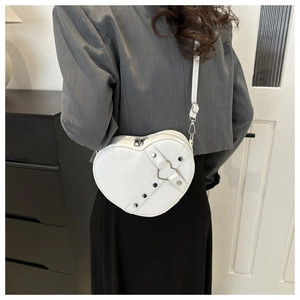 Detail van witte hartvormige crossbodytas met zilveren klinknagels en metalen gespontwerp