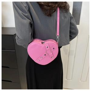 Detail van een roze hartvormige crossbodytas met metalen klinknagels en decoratieve riemen