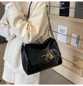 Detail einer glänzenden schwarzen Ledertasche mit Silberleiste und Metallkettenriemen