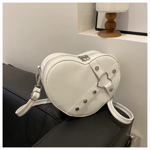 Detail van witte hartvormige schoudertas met zilveren studs op zwarte lederen bank