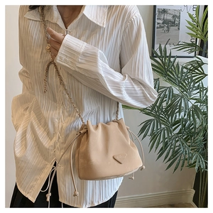 Detail van beige bucket bag met trekkoord, kettingriem en modieus driehoekig label