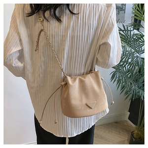 Detail van beige emmertas met trekkoord, gouden ketting en metalen logoplaatje