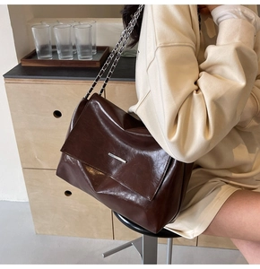 Detail einer dunkelbraunen Schultertasche mit Kettenriemen und silberner Metallschiene