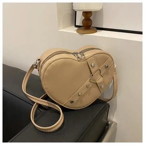 Detail van hartvormige beige crossbody tas met zilveren klinknagels en gespen