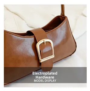 Close-up of shiny brown leather shoulder bag with a large gold plated hardware buckle