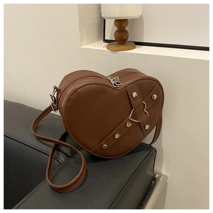 Detail van een bruine hartvormige crossbodytas met metalen klinknagels op de bank