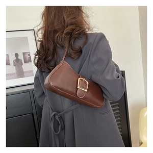 Detail of vintage brown leather baguette bag with oversized gold buckle on grey blazer
