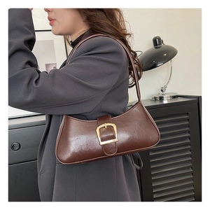 Detail of a brown crescent shoulder bag with glossy leather texture and golden buckle