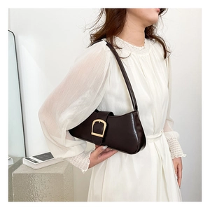 Detail of a dark brown underarm bag with a golden horseshoe buckle on a white dress