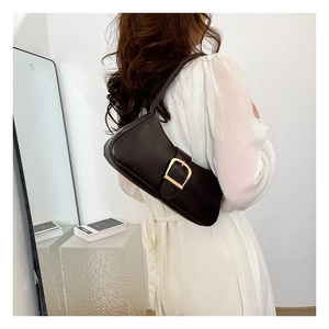 Detailed view of dark brown baguette bag with large gold buckle on white dress model