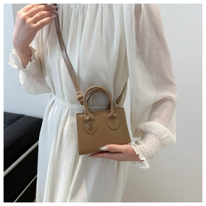 Close-up of mini brown leather crossbody bag styled with a white dress on a model