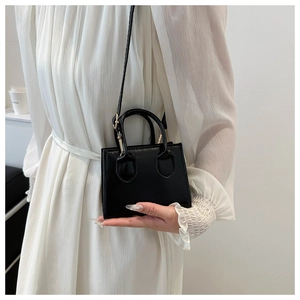 Detail of a minimalist black mini bag with gold metal buckles held by a model