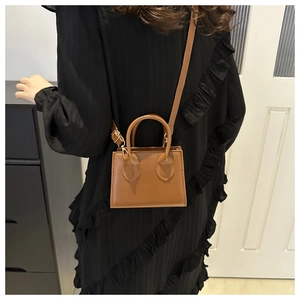 Detail of tan faux leather handbag featuring dual handles and thin adjustable shoulder strap