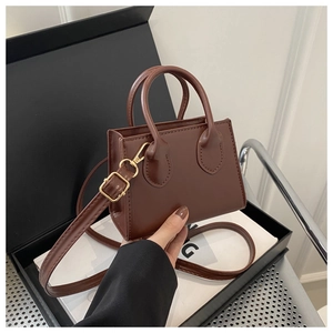 Close-up of brown mini tote bag with dual handles and gold-tone hardware in a gift box