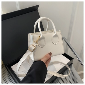Detail of white mini handbag with gold hardware and dual handles on black box