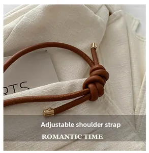 Detailed close-up of brown leather bag strap with adjustable knot and gold cylinder metal tips