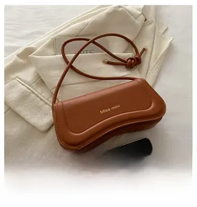 Detail of a brown leather shoulder bag with gold logo on a beige blazer background
