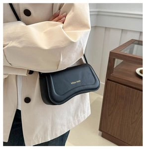 Detail of elegant black PU leather crossbody bag with gold lettering on a beige trench coat