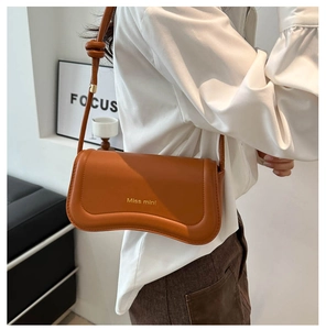Side view of caramel brown leather underarm bag with gold logo on a model with white shirt