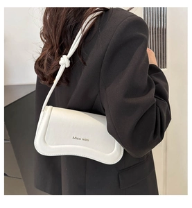Close-up of white shoulder bag featuring a wave-shaped flap and elegant knot strap detail