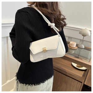 White underarm bag detail showing the long shoulder strap with knot and gold buckle