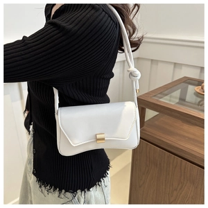 Close-up of white leather square bag with gold metal lock and knotted strap detail