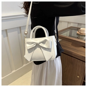 Close-up of a white bow shoulder bag with gold hardware worn by a model in a cozy setting