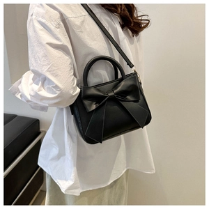 Detailed view of black handbag with large bow decoration and elegant curved handle