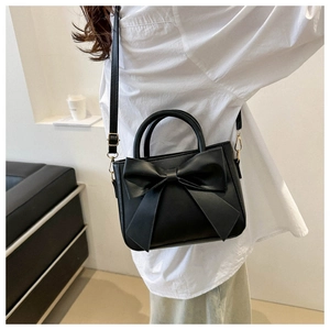 Detail of elegant black crossbody bag featuring a large leather bow and gold hardware