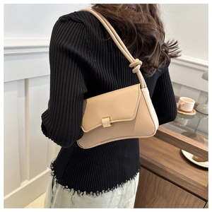 Minimalist beige leather shoulder bag with gold metal clasp shown on a model