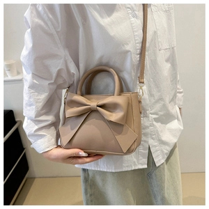 Detail of a beige square bag with a large bow showing shoulder strap and handle
