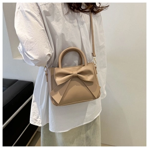Detail of beige shoulder bag with a large decorative bow and elegant gold-tone hardware