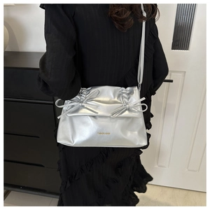 Detail of silver metallic tote bag featuring bow accents and ruched texture on shoulder strap