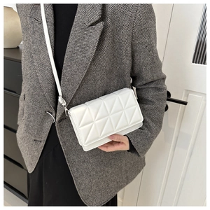 Detailaufnahme einer weißen geometrisch gesteppten Umhängetasche über einem grauen Blazer