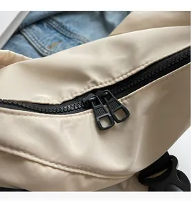 Detailed macro view of smooth dual metal zippers on a beige nylon crossbody dumpling bag