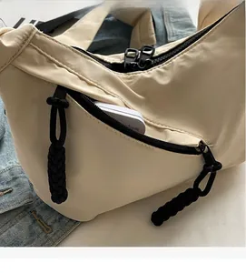 Detail of beige nylon half-moon bag featuring black wide zipper and functional front pocket