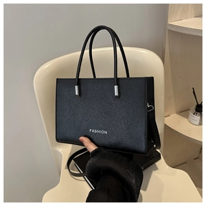 Détail d'un sac à main noir en cuir grainé avec logo Fashion sur une chaise blanche